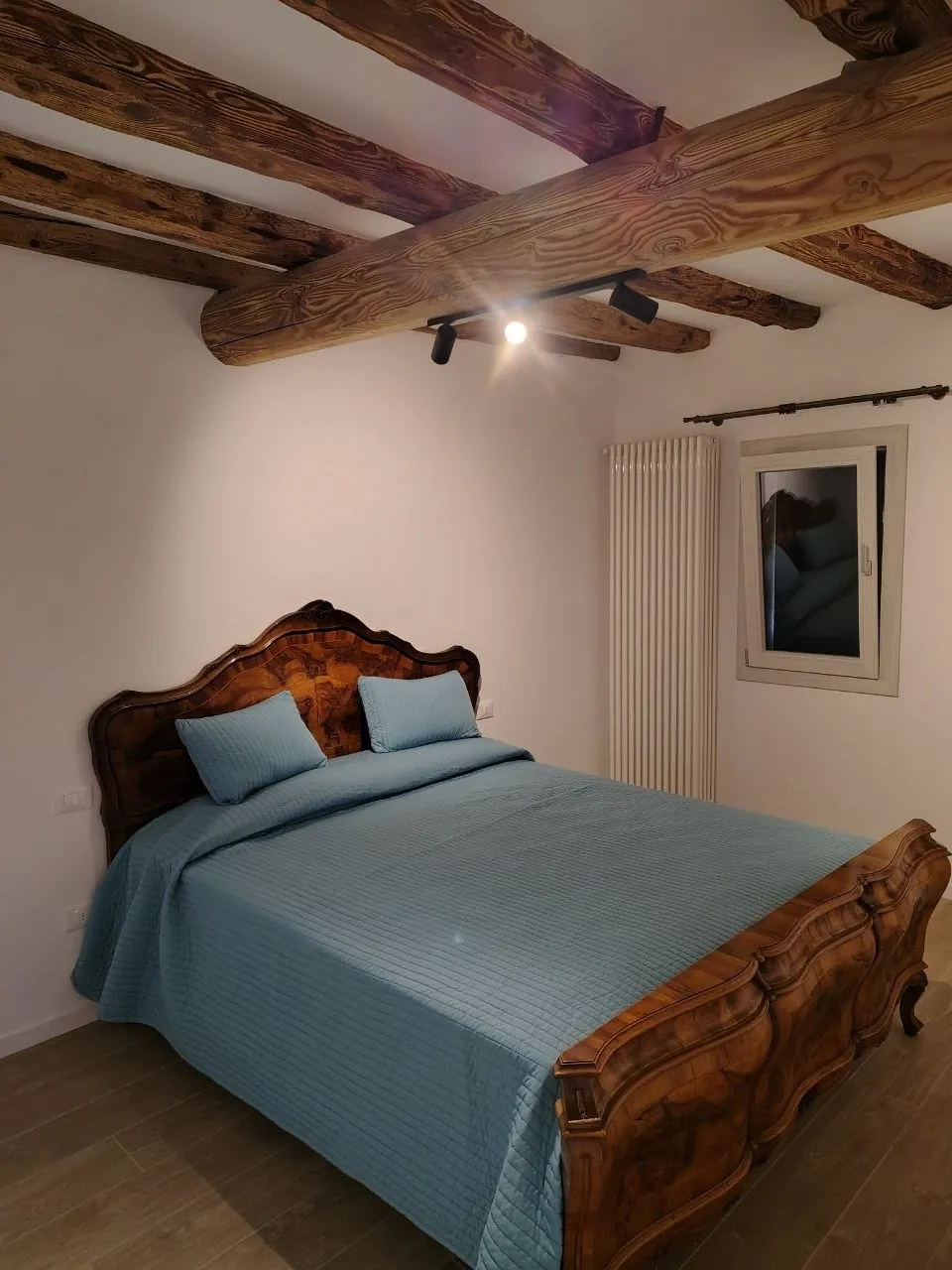 Camera matrimoniale con letto in noce intarsiato e travi a vista